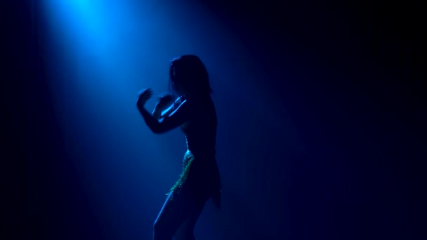 Silhouette d'une femme élancée aux cheveux longs qui danse passionnément des éléments de danses latino-américaines. Une danseuse pratique la salsa dans la lumière bleue du studio. Gros plan. — Video