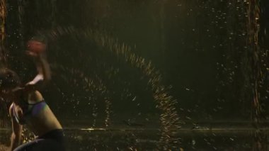 Genç bir atletik kadın, yağmurun altında inanılmaz derecede zor ve serin capoeira dövüş sanatları hareketleri sergiliyor. Akrobatik parkın yakın çekimi. Siluet. Yavaş çekim.