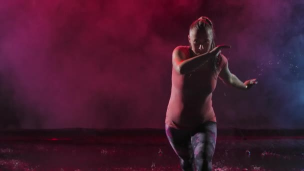 Νεαρή γυναίκα που εξασκείται στην Καποέιρα σε ένα σκοτεινό καπνιστό στούντιο στη βροχή. Μια πολεμική τέχνη που συνδυάζει στοιχεία χορού. Αργή κίνηση από κοντά. Σιλουέτα. — Αρχείο Βίντεο