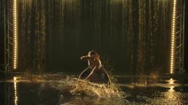 Formda bir dişinin silueti yağmurda karmaşık numaralar yapan ve çok fazla su sıçratan bir atlet-akrobat-capoeira 'dır. Sağlıklı yaşam tarzı, spor aşkı. Yavaş çekim.