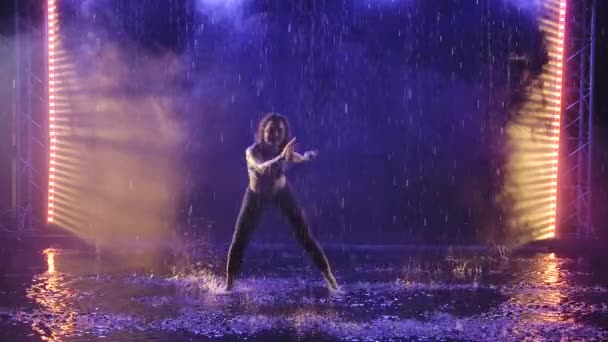 Une silhouette d'une femme sportive montrant la technique de l'art martial capoeira dans les rayons de lumière bleue sous les ruisseaux de pluie. Mouvement lent. — Video