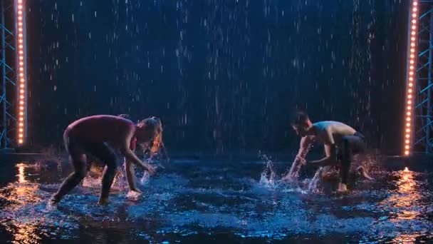 Un atlético y dos jóvenes practican la capoeira brasileña bajo la lluvia en un estudio oscuro. Parkour acrobático en la superficie del agua con salpicaduras. Silueta. Movimiento lento. — Vídeos de Stock