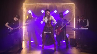 Genç bayan solist bir müzik grubuyla sahnede dururken mikrofona şarkı söylüyor. İrlanda tarzı kostümlü bir rock grubu karanlık bir arka plan ve mavi neon ışıklara karşı. Yavaş çekim.