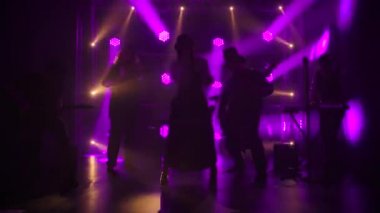 Orijinal İrlanda kostümlü ve şapkalı grup, dinamik mor ışıkların arkaplanına karşı karanlık bir stüdyoda gösteri yapıyor. Yavaş çekim.