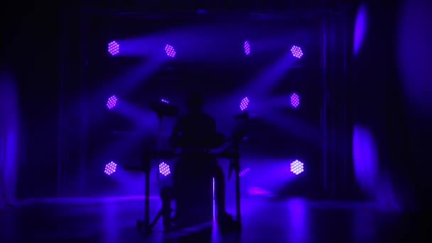 Mandlige trommeslager musiker spiller et musikinstrument i et mørkt studie på baggrund af blå lys. Koncert af et rockband på scenen, tromme. Silhuet. Langsom bevægelse. – Stock-video