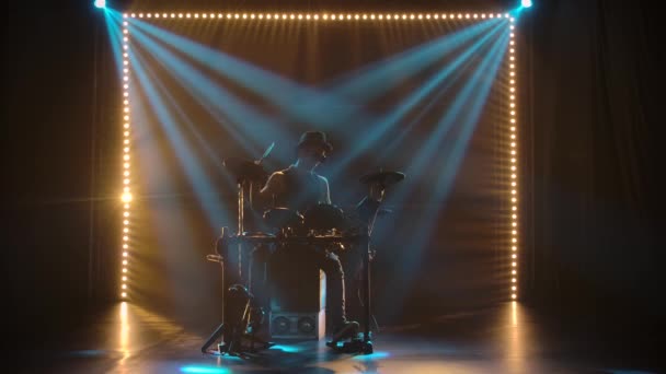 Een solo uitvoering door een drummer in een donkere studio in de stralen van blauw licht. Een silhouet van een man met drumstokken in een originele hoed speelt op een drumstel. Silhouetten. Langzame beweging. — Stockvideo