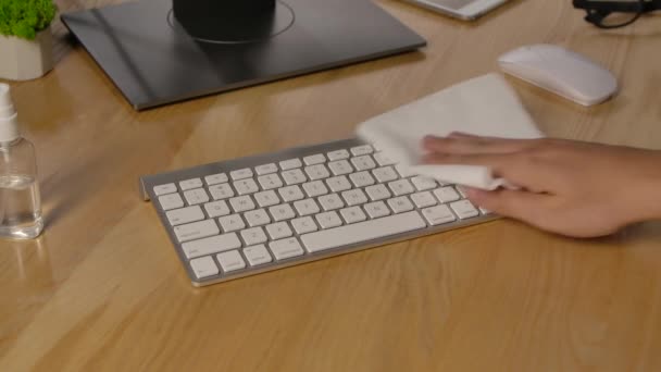Un homme vaporise de l'antiseptique sur une serviette et désinfecte un clavier d'ordinateur blanc, puis tape dessus. Quarantaine due au coronavirus. Précautions à prendre en cas d'éclosion de virus. Les mains en l'air. Mouvement lent. — Video