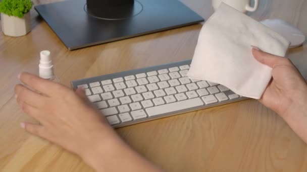 Uma mulher pulveriza anti-séptico em um guardanapo e desinfeta um teclado de computador branco. Quarentena devido ao coronavírus. Precauções para um surto de vírus. Fica em casa. Fica em segurança. Mãos ao alto. Movimento lento. — Vídeo de Stock