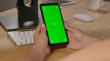 Krom anahtarlı yeşil ekranlı akıllı telefonu tutan bir kadının omuz manzarası. İçeriği dokunmadan veya aşırmadan tarıyor. Gadget ve modern insan konsepti. Kapatın. Yavaş çekim