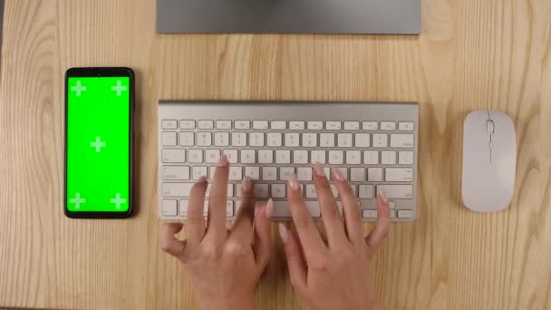 Geschäftsfrau tippt im Büro oder zu Hause auf der Tastatur. Smartphone mit grünem Bildschirm und Chroma-Taste mit vertikaler Bildschirmposition. Desktop-Ansicht. Hände in Nahaufnahme. Zeitlupe. — Stockvideo