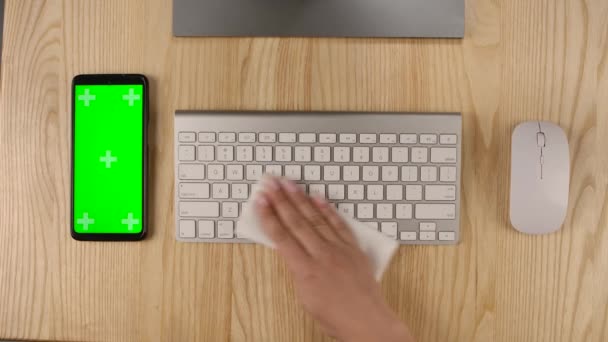 Uma mulher pulveriza um anti-séptico em um guardanapo e limpa um teclado de computador. Smartphone com tela verde e chave chroma com posição de tela vertical. Mãos ao alto. Movimento lento. — Vídeo de Stock