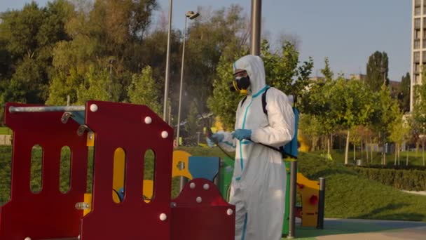 Un uomo in tuta protettiva disinfetta scivoli per bambini e attrazioni nel parco con spray chimici per prevenire la diffusione del coronavirus. COVID-19. Il concetto di pulizia. Chiudete. Rallentatore. — Video Stock