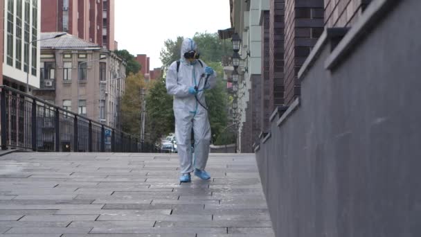 Viroloog in een beschermend pak desinfecteert het oppervlak, spuit vloeibare chemicaliën op de grond en muren op openbare plaatsen buiten. Langzame beweging. — Stockvideo