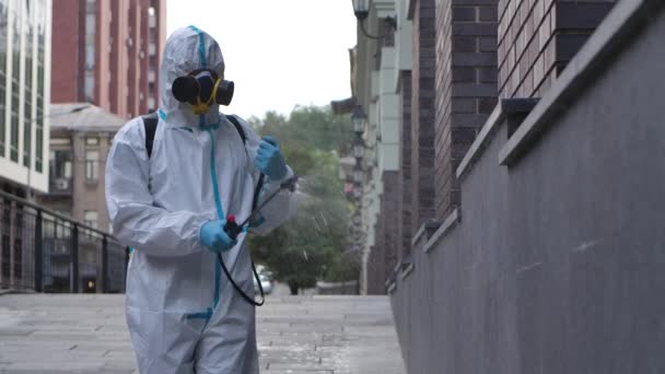 El virólogo con un traje protector desinfecta la superficie, rocía químicos líquidos en el suelo y paredes en lugares públicos afuera. En cámara lenta. De cerca.. — Vídeos de Stock