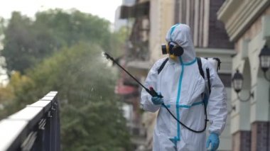 Koruyucu giysili profesyonel bir işçi şehrin sokaklarını koronavirüsten temizliyor. Hastalıkların yayılmasını önlemek için antibakteriyel kimyasalları dezenfekte eder. Salgın şehir. Kapatın. Yavaş çekim