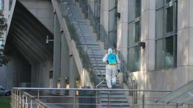 Koruyucu kıyafetli profesyonel bir temizlikçi ve solunum cihazı Covid-19 'u dezenfekte ediyor. Corona virüs dezenfeksiyonu. Tırabzanlara ve merdivenlere antiseptik dezenfektan sıkarak. Yavaş çekim.