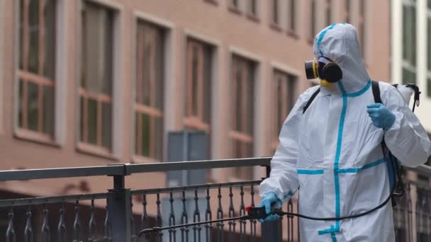Street cleaning with a pressure washer. A disinfector in protective suit and respirator disinfects handrails in a public place. A worker disinfects surfaces against coronavirus. Slow motion. Close up. — Stock Video
