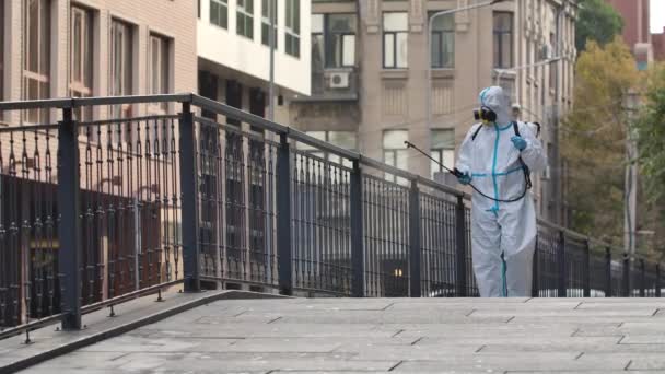 Limpieza de calles con una lavadora a presión. Un desinfectante con traje protector y respirador desinfecta las barandillas en un lugar público. Un trabajador desinfecta las superficies contra el coronavirus. Movimiento lento. — Vídeos de Stock