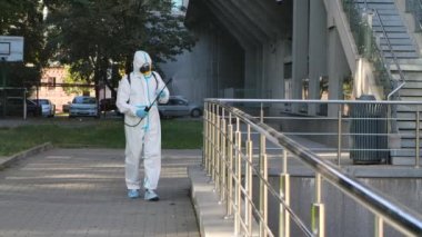 Tırabzanları dezenfekte eden adam. Corona virüsü grip dezenfeksiyonu. Coronavirus dezenfektanı. İşçiler beyaz üniforma giyer. Koruyucu giysi. Parmaklık spreyi dezenfektanı. Tehlikeli iş. Yavaş çekim.