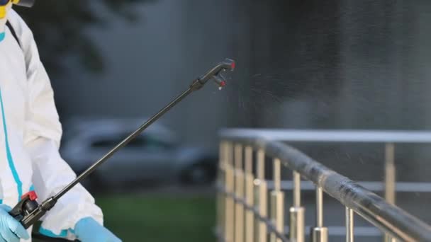 Hluboký veřejný čistič čistí zábradlí vysokotlakým dezinfekčním roztokem během pandemie koronaviru. Ten muž má na sobě ochranný oblek, rukavice a respirátor. Zavřít. Zpomalený pohyb. — Stock video