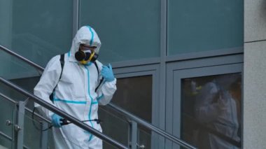 Koruyucu giysili bir adam antiseptik spreyle sokağı dezenfekte ediyor. Koronavirüs hastalığından dolayı yüzey tedavisi. Virüs salgını ve koruma kavramları. Kapatın. Yavaş çekim.