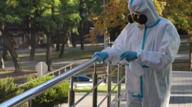 Koruyucu kıyafet giyen bir virüs uzmanı koronavirüs salgını sırasında korkulukları antiseptik sprey ve mendille dezenfekte ediyor. Ağır çekim. Kapat..