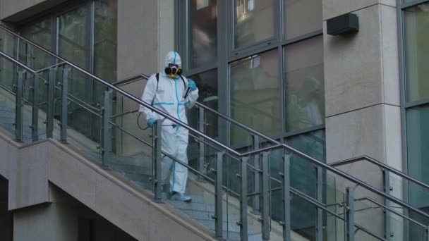 El desinfectante en el traje protector trata el territorio de las calles de la ciudad, rocía el desinfectante antibacteriano. Desinfección de lugares públicos, barandillas, pasos de coronavirus. Movimiento lento. — Vídeo de stock