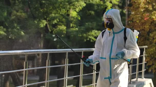 L'uomo in una tuta protettiva bianca disinfetta corrimano e ringhiere in un'area pubblica su una strada deserta. Il lavoratore utilizza un disinfettante antibatterico ad alta pressione. Al rallentatore. Da vicino.. — Video Stock