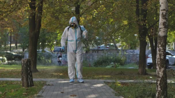 Virologist in a white protective suit disinfects paving slabs in a public park. The man uses a high pressure antiseptic solution. Cleaning concept. Slow motion. — Stock Video