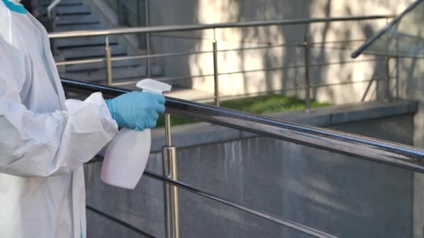 Un jeune hygiéniste portant une combinaison de protection et un respirateur nettoie et désinfecte les surfaces des mains courantes avec un spray antibactérien. Au ralenti. Gros plan. — Video