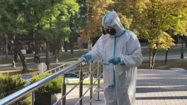 Ein Virologe in Schutzkleidung desinfiziert das Geländer bei einem Coronavirus-Ausbruch mit einem antiseptischen Spray und einem Gewebe. Zeitlupe. Nahaufnahme. — Stockvideo