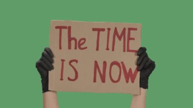 Siyah eldivenli bilinmeyen birinin elleri karton bir poster kaldırıyor. Şimdi tam zamanı. Eşitlik ve birlik kavramı. Yeşil ekran, krom anahtar. Kapatın. Yavaş çekim.