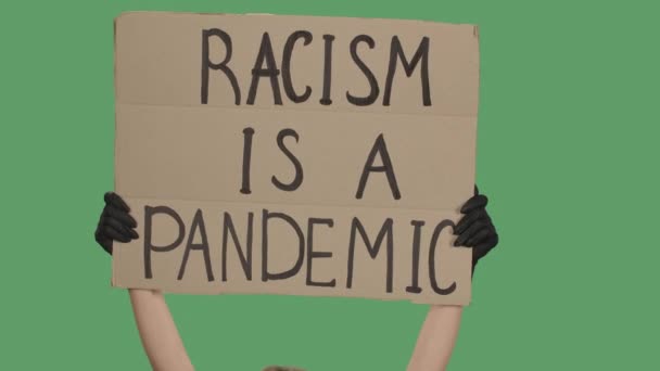 Una persona sconosciuta sta tenendo un manifesto da una scatola di cartone con le parole RACISM IS A PANDEMIC with both hands. Uguaglianza e unità. Isolato uno schermo verde, chiave cromatica. Chiudete. Rallentatore. — Video Stock