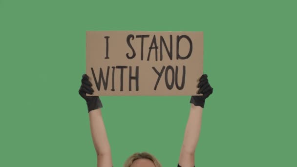 Blonde Frau, die mit beiden Händen ein Poster aus einem Karton hält, auf dem steht: "Ich STAND WITH YOU". Rassismus gegen Schwarze. Isoliert ein grüner Bildschirm, Chroma-Taste. Aus nächster Nähe. Zeitlupe. — Stockvideo