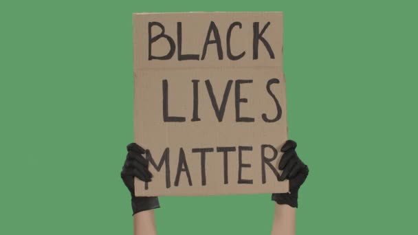 Le mani di una persona sconosciuta in guanti neri sollevano un poster di cartone BLACK LIVES MATTER. Uguaglianza e unità. Isolato uno schermo verde, chiave cromatica. Chiudete. Rallentatore. — Video Stock