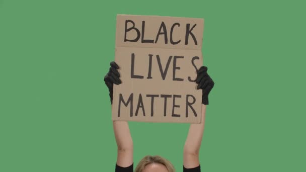 Mujer rubia sosteniendo sobre la cabeza un póster de una caja de cartón con las palabras BLACK LIVES MATTER con ambas manos. Concepto de igualdad y unidad. Aislado una pantalla verde, croma key. De cerca. Movimiento lento. — Vídeo de stock