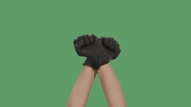 Перехрещені руки в чорних рукавицях з стиснутими кулаками піднімаються до зеленого екрану, хроматичного ключа. Невпізнавана жінка показує жест свободи. Протести і бунти. Расизм - відсутність расизму. Закрийся. Повільний рух. — стокове відео