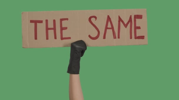 Рука в чорних рукавичках піднімає картонний плакат "S SAME". Концепція рівності та єдності. Багатогранність насильства та античорного расизму. Ізольований зелений екран, ключ хроми. Близько. Повільний рух . — стокове відео