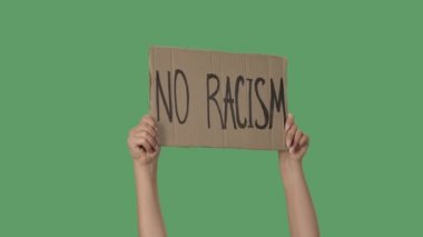 Üzerinde RACISM HAYIR yazan bir protesto posteri. İnsan hakları hareketini resmetmek için arka plan. Poster yeşil ekranı tutan kadın eller, kroma anahtar. Kapatın. Yavaş çekim.