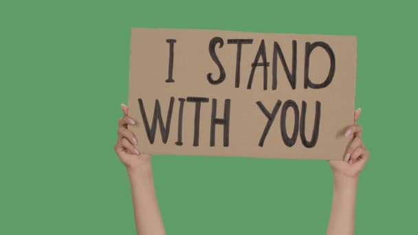 Kvinnliga händer håller en affisch från en pappkartong med orden I STAND WITH. Protester mot rasism och polisbrutalitet. Isolerade en grön skärm, kromnyckel. Närbild. Långsamma rörelser. — Stockvideo