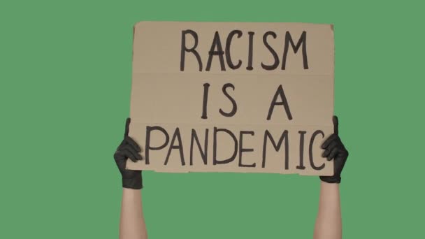 Üzerinde RACISM yazan karton posteri göstermek bir pandemiktir. İnsan Hakları Gösterisi. Ellerinde yeşil ekran, krom anahtar olan bir poster var. Kapatın. Yavaş çekim. — Stok video