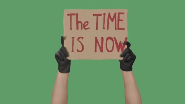 Female hands in black gloves pick up a poster from a cardboard box that reads THE TIME IS NOW. Cardboard banner. Isolated a green screen, chroma key. Close up. Slow motion. — Stock Video