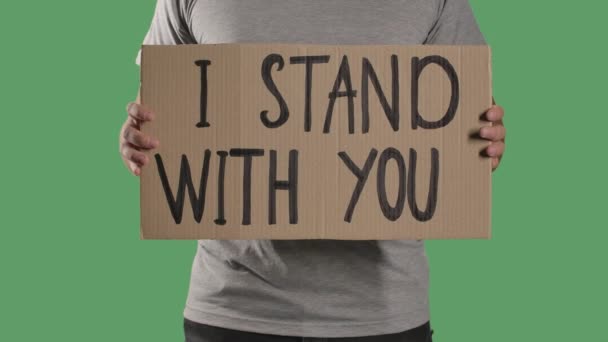 Man holds in front of him a poster from a cardboard box with the words I STAND WITH YOU. Protest against police brutality terror and racism. Isolated a green screen, chroma key. Close up. Slow motion — Stock Video
