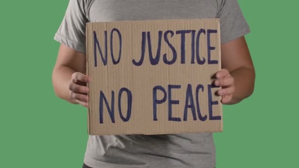 Egy férfi tart maga előtt egy posztert egy kartondobozból azzal a felirattal, hogy NEM JUSTICE NO PEACE. A sztrájk és a rasszizmus fogalma. Elkülönített egy zöld vásznat, krómkulcsot. Közelről. Lassú mozgás.. — Stock videók