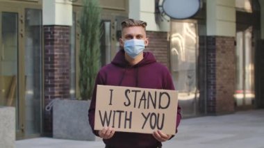 Tıbbi maske takan beyaz erkek protestocu seninle durduğum sloganın yazılı olduğu bir karton poster tutuyor. Irkçılık kavramını bırak. Ağır çekim. Açık hava portresini kapat..