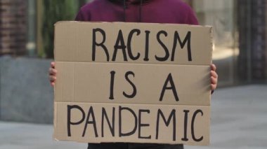 RACISM, Afrika kökenli bir Amerikan hakları savunucusunun elindeki mukavva bir posterin üzerindeki bir pandemiktir. Poster ve elin yakın çekimi. Irkçılık yapma, ırkçılık yapma. Yavaş çekim.