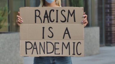 RACISM, kadın protestocuların elindeki karton posterdeki bir pandemiktir. Poster ve elin yakın çekimi. Irkçılık yapma, ırkçılık yapma. Şehir sokak protestosu. Yavaş çekim.