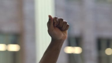 Afro-Amerikan erkek elini kaldırdı ve kenetlenmiş yumruğuyla şehrin arka planını protesto etti. Irkçılığa ve polis zulmüne karşı protesto. Kapatın. Yavaş çekim.
