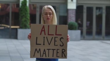Açık havada, elinde karton bir poster tutan genç beyaz bir kadın aktivistin portresi. Üzerinde 