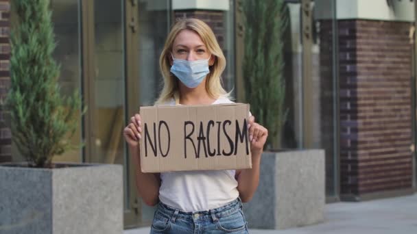 Jovem mulher branca uma máscara médica segurando cartaz de papelão com slogan escrito sem racismo. Conceito da greve e anti racista.Ao ar livre Black Lives Matter. Movimento lento. Fechar. — Vídeo de Stock